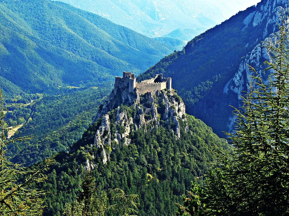 Vue aérienne spectaculaire du château de Puilaurens niché au sommet d'un piton rocheux, entouré de montagnes verdoyantes dans l'Aude.